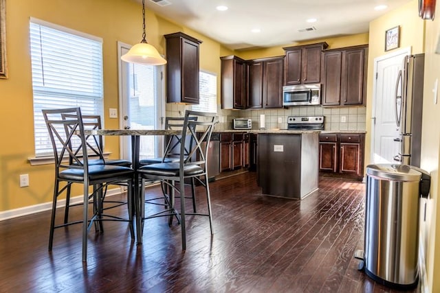 kitchen featuring dark brown cabinetry, tasteful backsplash, dark hardwood / wood-style flooring, decorative light fixtures, and appliances with stainless steel finishes