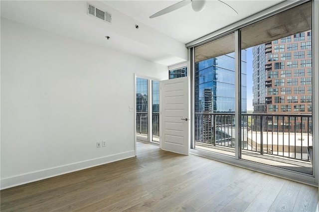 spare room with expansive windows, visible vents, wood finished floors, and a healthy amount of sunlight