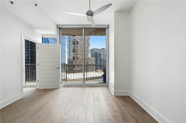 unfurnished room featuring a city view, expansive windows, wood finished floors, baseboards, and ceiling fan