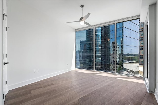 unfurnished room with floor to ceiling windows, a ceiling fan, baseboards, and wood finished floors