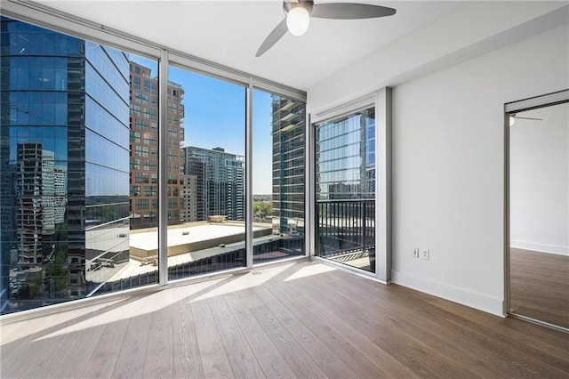 empty room with a wall of windows, baseboards, ceiling fan, wood finished floors, and a view of city