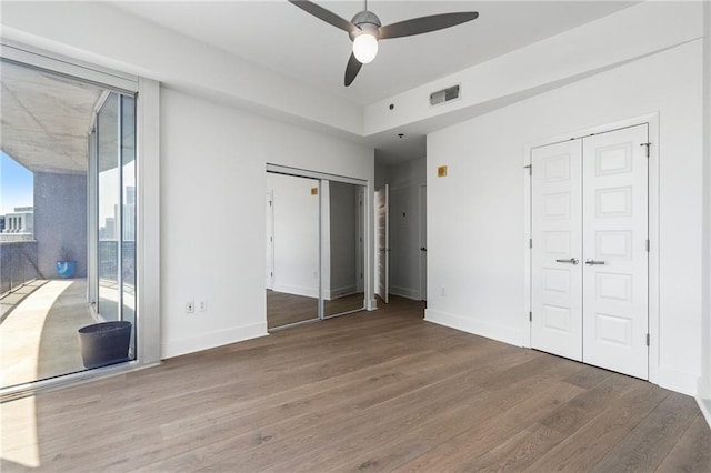 unfurnished bedroom featuring baseboards, multiple closets, visible vents, and wood finished floors