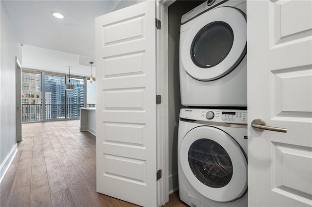 laundry area with recessed lighting, wood-type flooring, baseboards, stacked washing maching and dryer, and laundry area