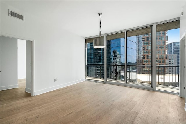 unfurnished room featuring a city view, a wall of windows, wood finished floors, baseboards, and visible vents