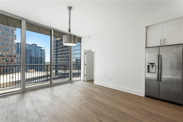 unfurnished dining area featuring wood finished floors, baseboards, a view of city, and a wall of windows