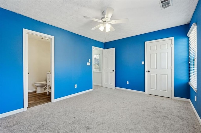 unfurnished bedroom featuring ceiling fan, ensuite bathroom, light carpet, and a textured ceiling