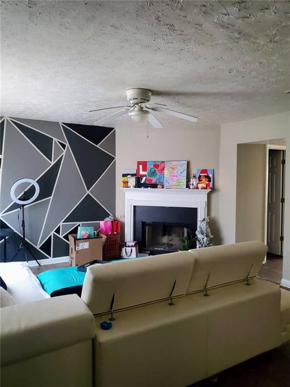 living room featuring a fireplace, a textured ceiling, and ceiling fan