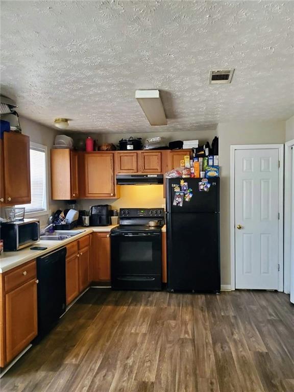 kitchen featuring dark wood-type flooring, visible vents, under cabinet range hood, and black appliances