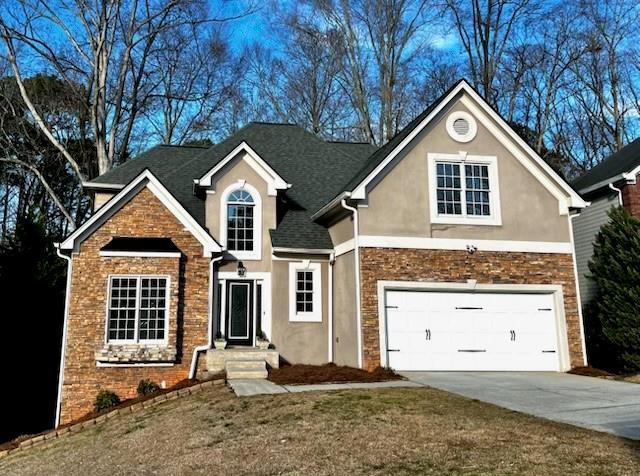 traditional home with a garage, stone siding, driveway, and a front lawn