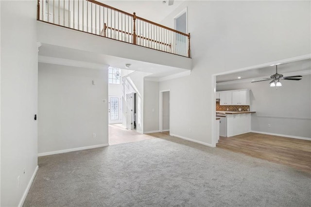 unfurnished living room featuring baseboards, light carpet, ceiling fan, and a high ceiling