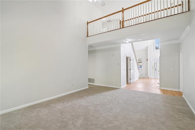 unfurnished living room with a high ceiling, visible vents, baseboards, ornamental molding, and carpet