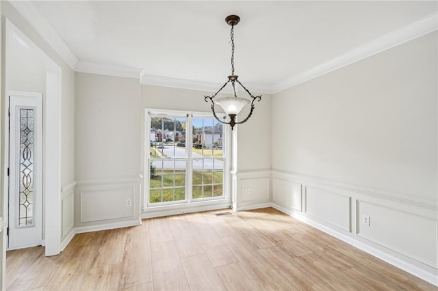 unfurnished dining area featuring wainscoting, ornamental molding, an inviting chandelier, light wood-style floors, and a decorative wall