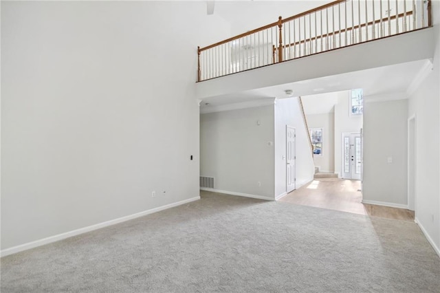 unfurnished living room with a high ceiling, carpet flooring, visible vents, and baseboards