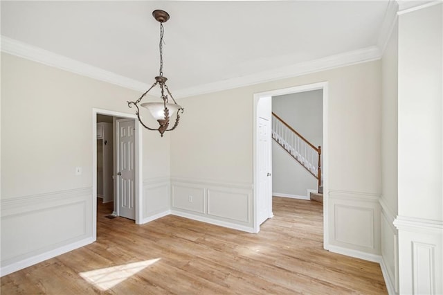 unfurnished dining area featuring a decorative wall, light wood-style floors, stairs, ornamental molding, and wainscoting