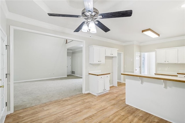 kitchen with a kitchen breakfast bar, light wood-style floors, white cabinetry, and crown molding