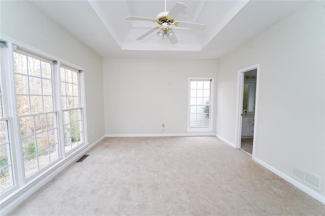 empty room with light carpet, baseboards, visible vents, and a raised ceiling