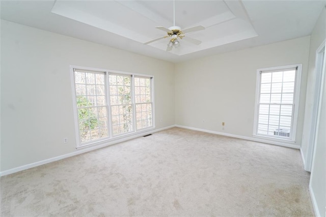 carpeted empty room with a ceiling fan, a raised ceiling, visible vents, and baseboards