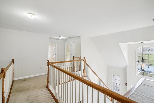 corridor with baseboards, carpet flooring, a notable chandelier, and an upstairs landing