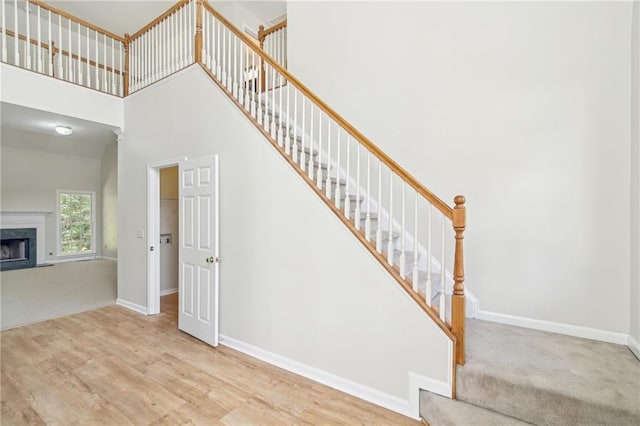 staircase featuring a towering ceiling, a premium fireplace, baseboards, and wood finished floors