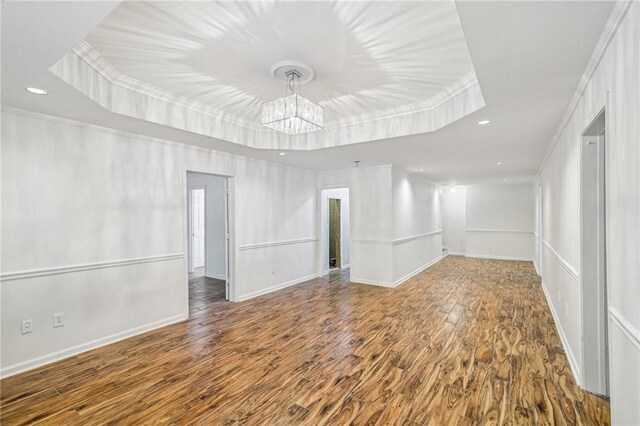 empty room featuring ornamental molding, a tray ceiling, baseboards, and wood finished floors