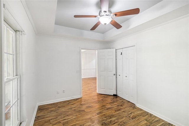 unfurnished bedroom featuring wood finished floors, baseboards, a closet, a tray ceiling, and crown molding