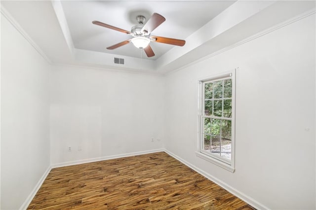 unfurnished room with a tray ceiling, wood finished floors, visible vents, and baseboards