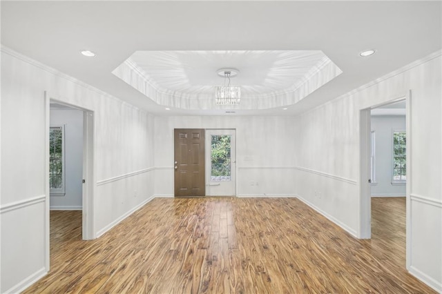 empty room with an inviting chandelier, crown molding, a raised ceiling, and wood finished floors