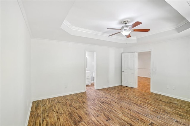 unfurnished room with baseboards, wood finished floors, a raised ceiling, and crown molding