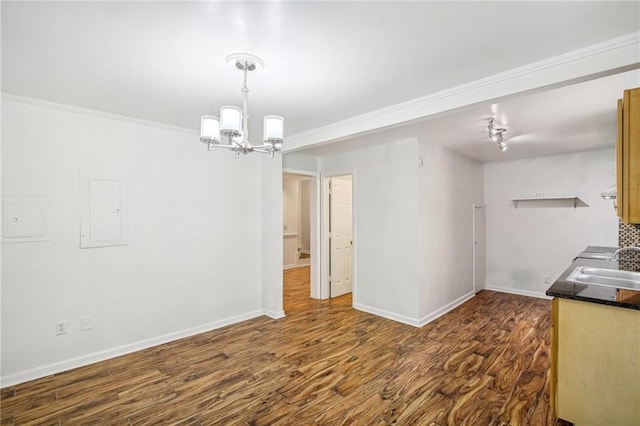 unfurnished dining area featuring a chandelier, dark wood-style flooring, a sink, baseboards, and ornamental molding