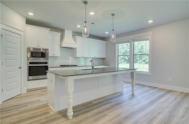 18 Slick Ct, Senoia, GA 30276 - kitchen with stainless steel appliances, custom exhaust hood, tasteful backsplash, white cabinetry, and an island with sink