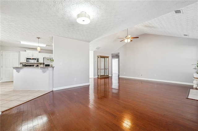 unfurnished living room featuring ceiling fan, lofted ceiling, a textured ceiling, and hardwood / wood-style flooring