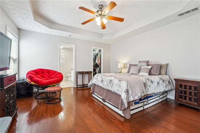 bedroom with a raised ceiling, a spacious closet, a textured ceiling, and dark wood-type flooring