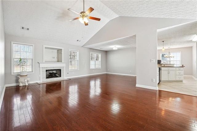 unfurnished living room featuring hardwood / wood-style flooring, a tiled fireplace, vaulted ceiling, ceiling fan with notable chandelier, and sink