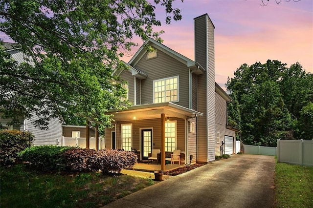 traditional-style home featuring a chimney, covered porch, fence, a garage, and driveway