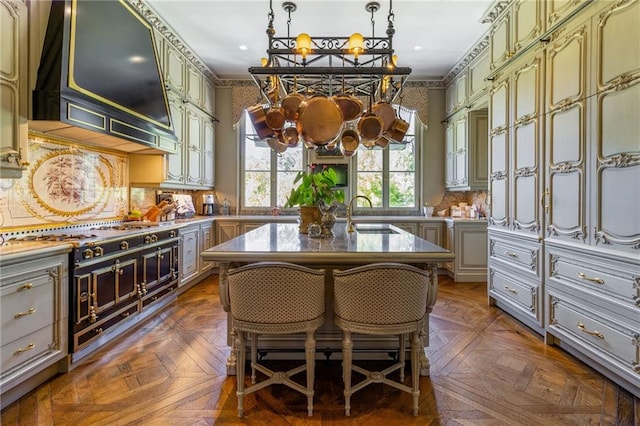 kitchen with wall chimney range hood, dark parquet floors, a center island with sink, backsplash, and a kitchen breakfast bar