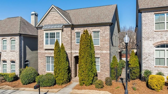 townhome / multi-family property featuring fence, roof with shingles, a standing seam roof, brick siding, and metal roof