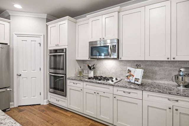 kitchen with tasteful backsplash, light stone countertops, appliances with stainless steel finishes, wood finished floors, and white cabinetry