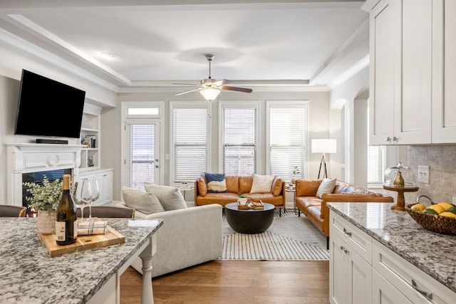 living area featuring ornamental molding, arched walkways, a fireplace, ceiling fan, and dark wood-style flooring