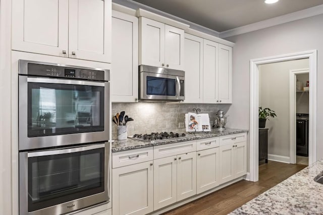 kitchen with dark wood finished floors, ornamental molding, light stone counters, decorative backsplash, and appliances with stainless steel finishes