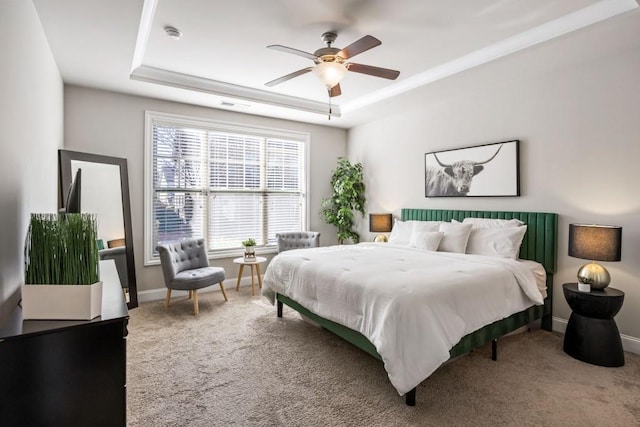 carpeted bedroom with ceiling fan, a raised ceiling, and baseboards