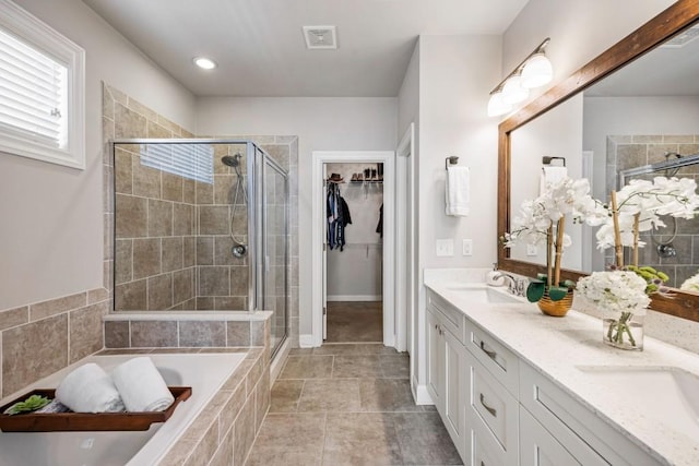 full bathroom featuring a shower stall, a spacious closet, double vanity, and a sink