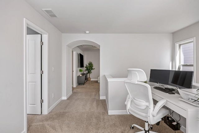 office space with baseboards, visible vents, arched walkways, and light carpet