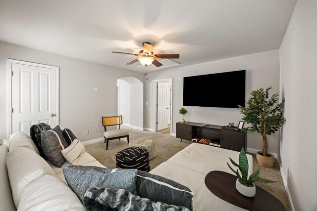 carpeted living area featuring a ceiling fan, baseboards, and arched walkways