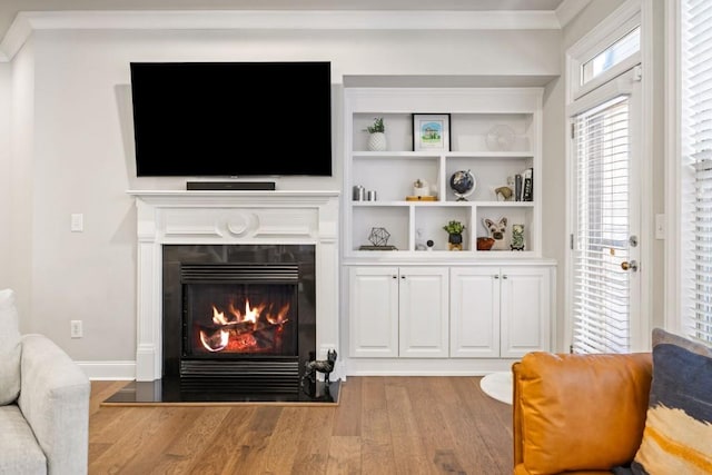 living area with ornamental molding, a warm lit fireplace, baseboards, and wood finished floors