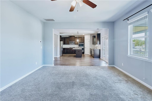 unfurnished living room with a ceiling fan, baseboards, visible vents, and carpet flooring