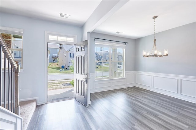 foyer entrance featuring a wainscoted wall, visible vents, stairway, wood finished floors, and a chandelier