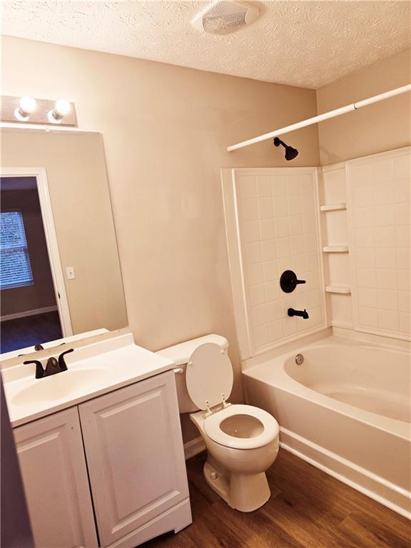 full bathroom featuring vanity, wood-type flooring, a textured ceiling, shower / bathtub combination, and toilet