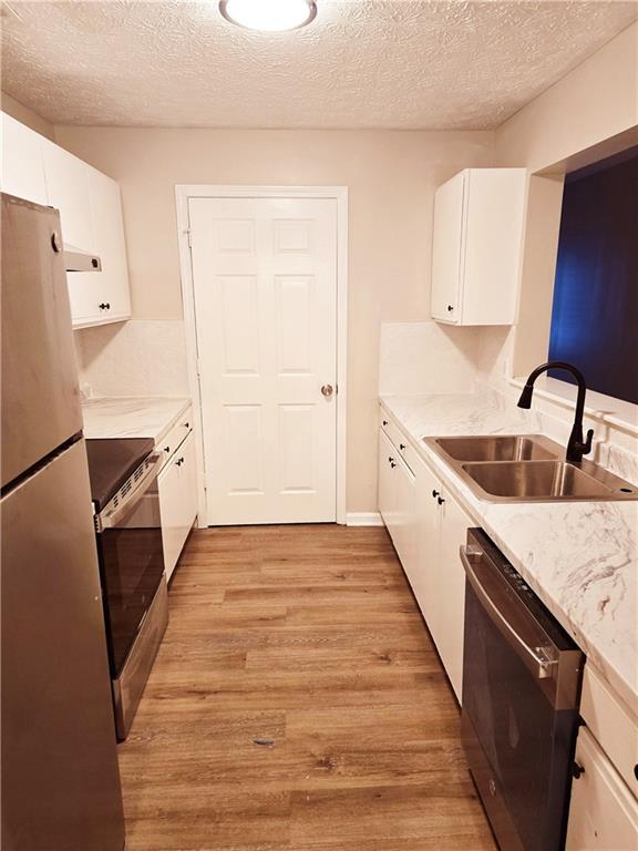 kitchen with sink, a textured ceiling, light wood-type flooring, appliances with stainless steel finishes, and white cabinets