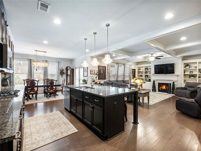 kitchen with appliances with stainless steel finishes, pendant lighting, an island with sink, sink, and dark stone countertops