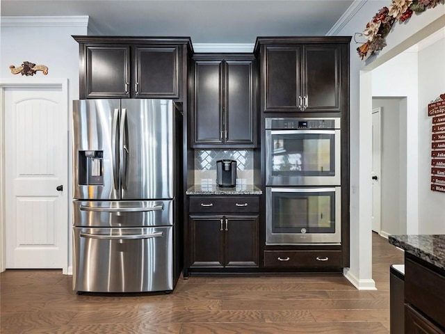 kitchen featuring appliances with stainless steel finishes, dark hardwood / wood-style floors, backsplash, dark stone counters, and crown molding